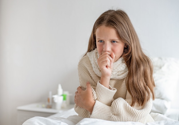 Porträt eines schönen Mädchens mit einer Temperatur sitzt auf dem Bett und hustet