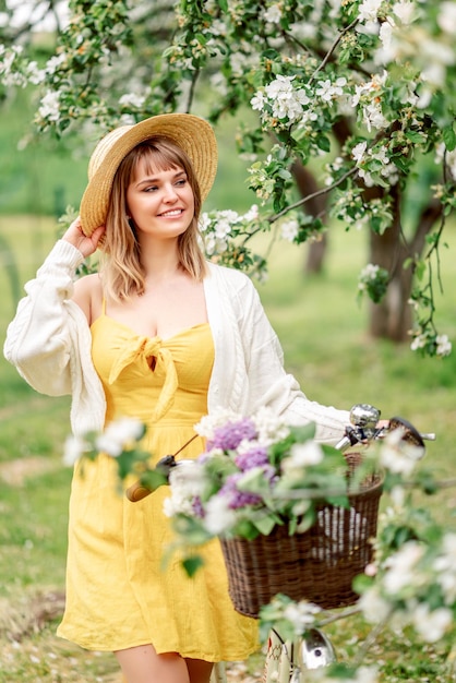 Porträt eines schönen Mädchens mit Hut auf einem Fahrrad in einem blühenden Garten Frühlingsfoto.