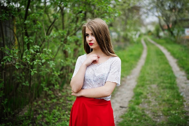 Porträt eines schönen Mädchens mit roten Lippen im Frühlingsblütengarten auf rotem Kleid und weißer Bluse