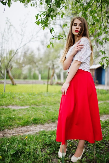 Porträt eines schönen Mädchens mit roten Lippen im Frühlingsblütengarten auf rotem Kleid und weißer Bluse