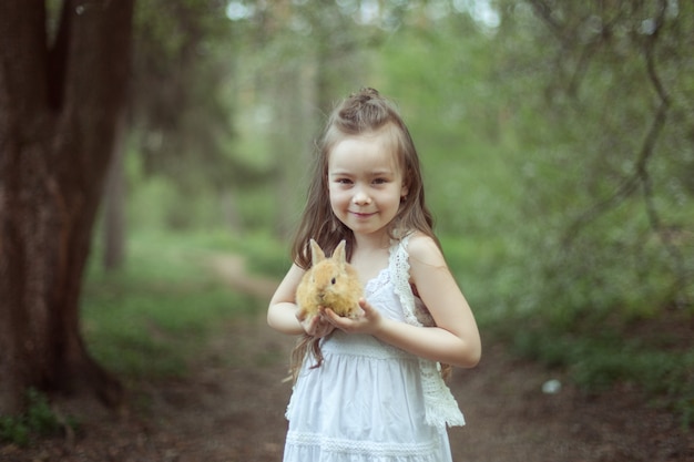 Porträt eines schönen niedlichen Mädchens im Wald. In den Händen eines Mädchens, das ein rotes Kaninchen hält.