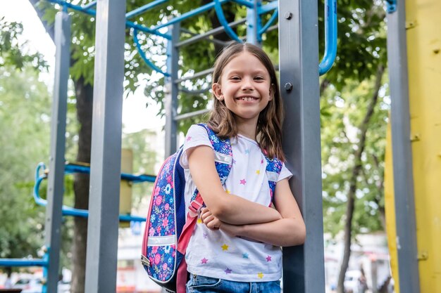 Foto porträt eines schönen schulmädchens mit rucksack, das auf dem spielplatz bleibt