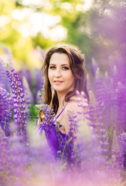 Porträt eines schönen schwangeren Mädchens in einem lila Sommerkleid Eine Frau auf dem Hintergrund der Lupinen