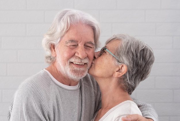 Porträt eines schönen Seniorenpaares, das seine Frau umarmt, küsst ihren Ehemann, der zu Hause steht