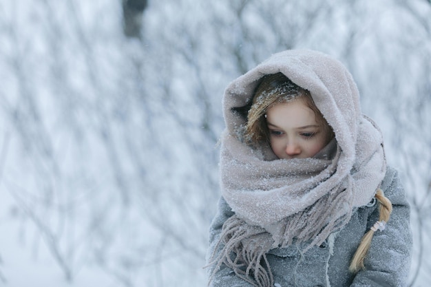 Foto porträt eines schönen süßen kleinen kindes in einem schal im wald im winter mit schnee und schneesturm