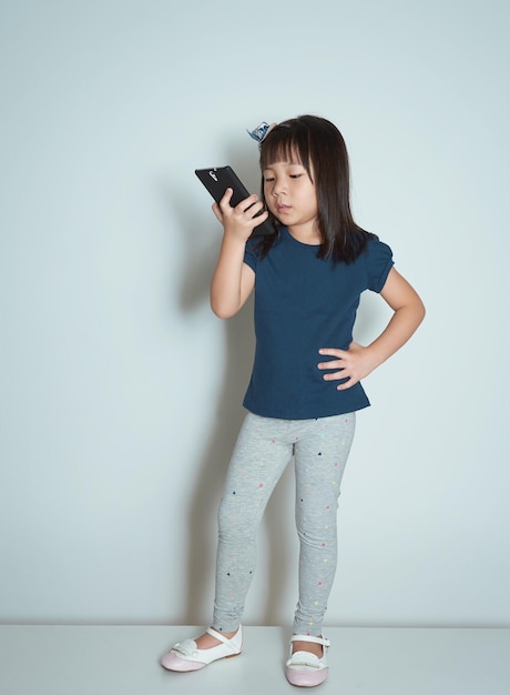 Porträt eines schönen und glücklichen asiatischen kleinen Mädchens, das einen Anruf auf einfachem Hintergrund macht