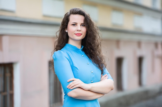 Porträt eines schönen weißen europäischen brünetten Mädchens, das im Sommer ein blaues Kleid auf der Straße trägt