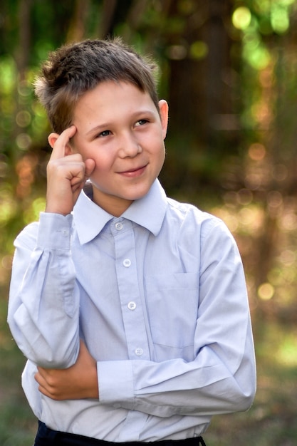 Porträt eines Schuljungen, der vor einem verschwommenen Hintergrund grüner Bäume nachdenklich zur Seite schaut