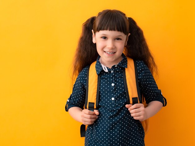 Porträt eines Schulmädchens mit einem Rucksack auf gelbem Hintergrund