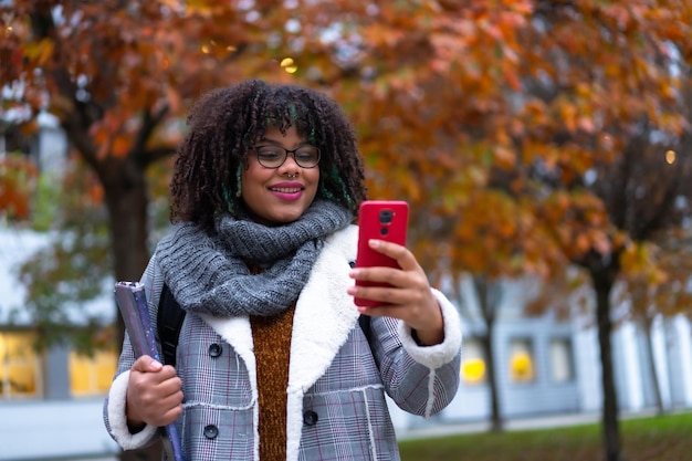 Porträt eines schwarzen ethnischen Mädchens, das im Herbst in der Hochschule spaziert und zurück zur Schule telefoniert