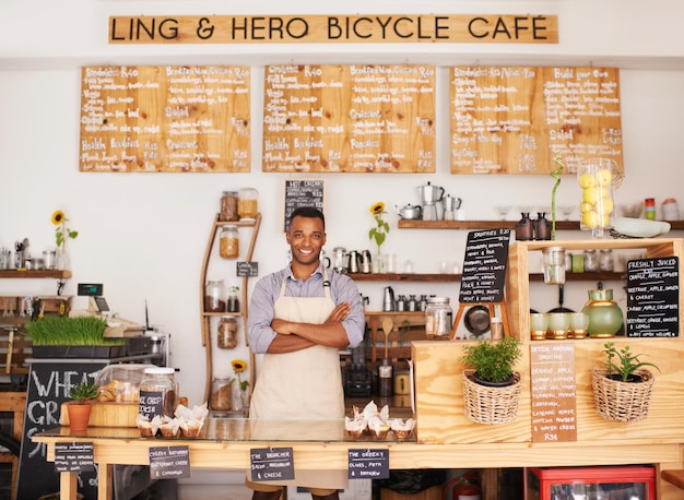 Porträt eines schwarzen Mannes und eines Barista mit verschränkten Armen im Café voller Stolz auf Karriere oder Job. Kellnerlächeln und Selbstvertrauen einer Afrikanerin aus Nigeria in einem Restaurant, einem kleinen Unternehmen und einem Café