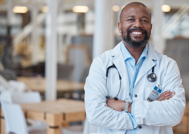 Porträt eines schwarzen Mannes und eines glücklichen Arztes mit verschränkten Armen im Krankenhaus für die Gesundheitsfürsorge. Gesicht eines afrikanischen Mediziners und eines Chirurgen oder selbstbewussten Mitarbeiters aus Nigeria mit einem Lächeln für das Wohlbefinden