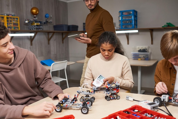 Porträt eines schwarzen Teenagermädchens, das Roboter mit verschiedenen Gruppen von Kindern im Ingenieurunterricht an der modernen Schule baut