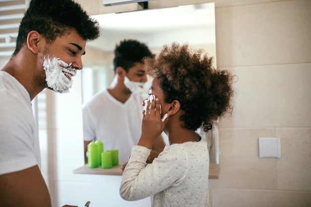Porträt eines schwarzen Vaters und einer Tochter, die sich im Badezimmer mit Rasierschaum amüsieren