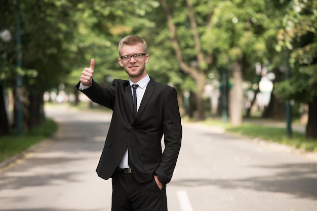 Porträt eines selbstbewussten Geschäftsmannes, während er draußen im Park steht und Daumen nach oben zeigt