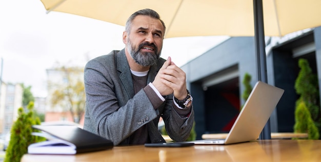 Porträt eines seriösen Geschäftsmannes mit Laptop im Stadtcafé, der online arbeitet