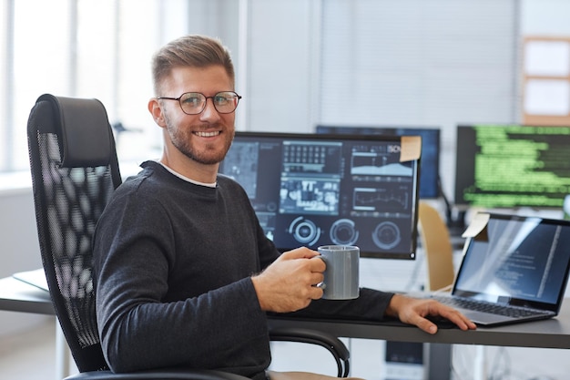 Foto porträt eines softwareprogrammierers, der in die kamera lächelt, während er am arbeitsplatz im büro mit kaffee cu posiert