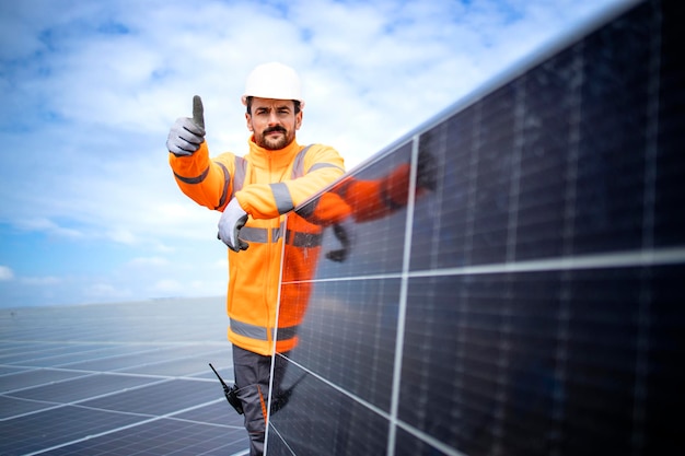 Porträt eines Solarenergiearbeiters, der ein Photovoltaikpanel hält und in einem Solarkraftwerk steht