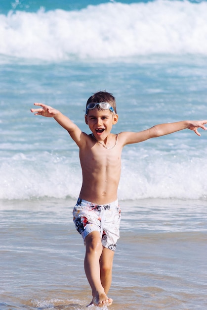 Porträt eines spielerischen Jungen, der am Strand am Ufer spazieren geht