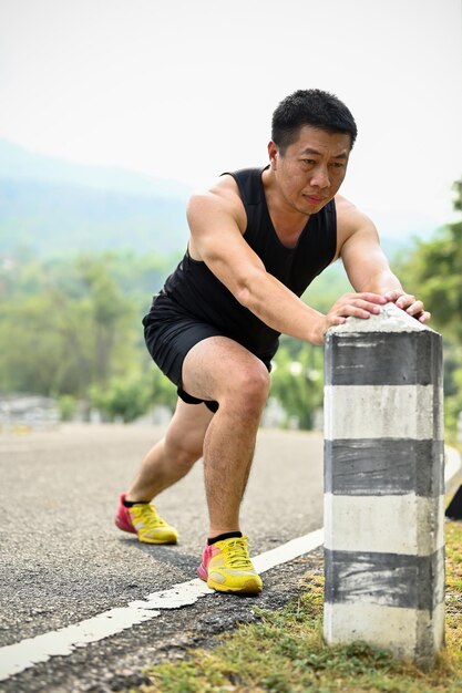 Porträt eines sportlichen asiatischen Mannes in Sportkleidung, der seine Beine ausstreckt, bevor er in einem Park läuft