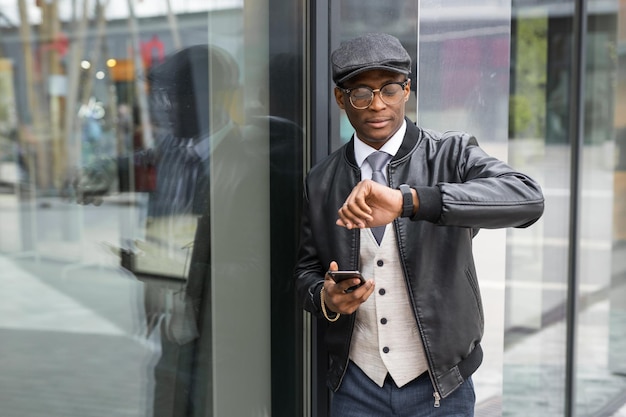 Porträt eines stilvollen afrikanischen Mannes mit Smartphone, der auf die Uhr schaut