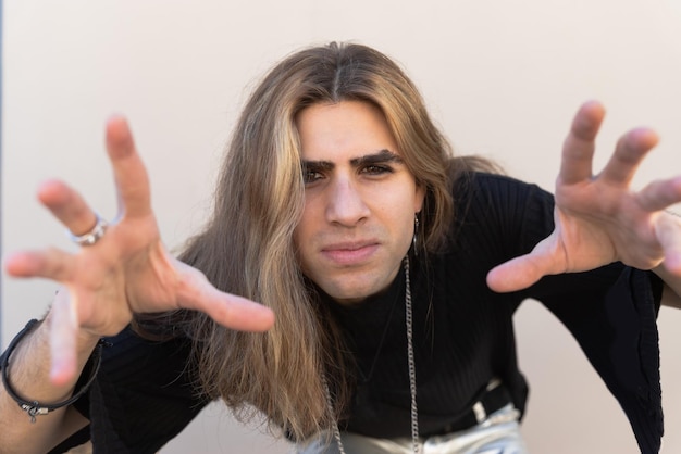 Foto porträt eines stilvollen hipsters mit langen haaren und eyeliner, der handgesten macht