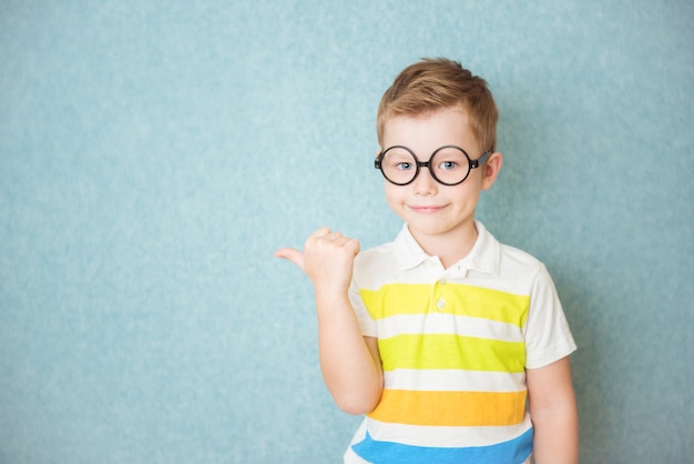 Porträt eines stilvollen kleinen Jungen mit Fingerfinger an Punkten in der Seite. Kind auf blauer Tafel. Erfolg, helle Idee, kreative Ideen und innovatives Technologiekonzept