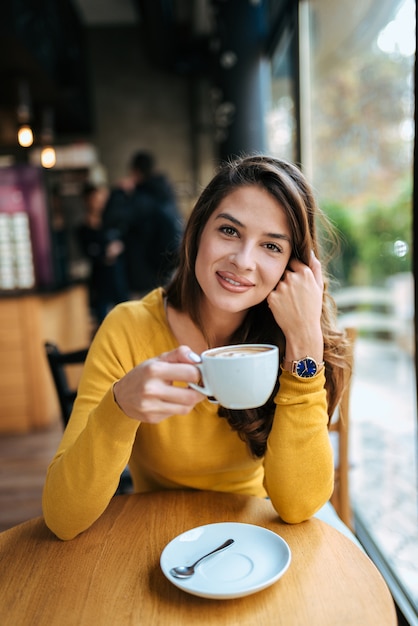 Porträt eines stilvollen trinkenden kaffees der jungen frau im café, kamera betrachtend.