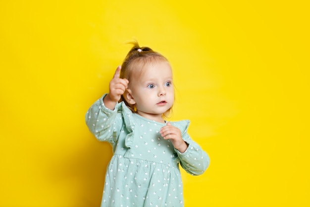 Porträt eines süßen Babys mit blauen Augen auf gelbem Hintergrund zeigt zur Seite. Ein Platz für Texte.