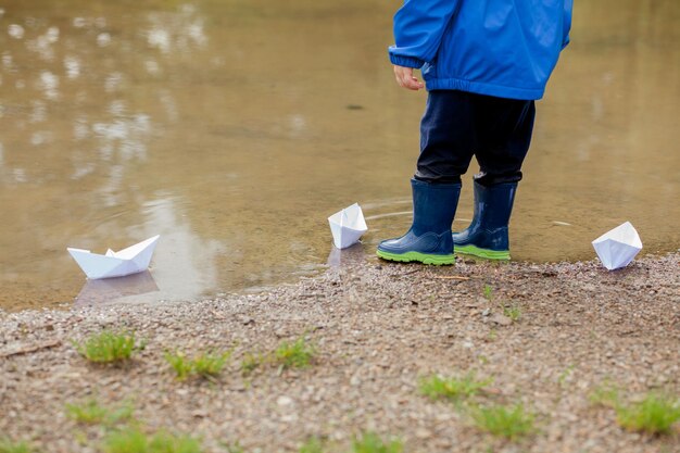 Porträt eines süßen Jungen, der mit einem handgefertigten Schiffskindergartenjungen spielt, der ein Spielzeugboot am Rand des Wassers im Park segelt