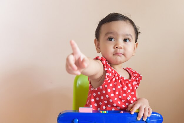 Porträt eines süßen kleinen asiatischen Mädchens, das in Rot gekleidet ist und mit dem Finger nach vorne zeigt, isoliert auf dem Hintergrundbaby-Ausdruckskonzept