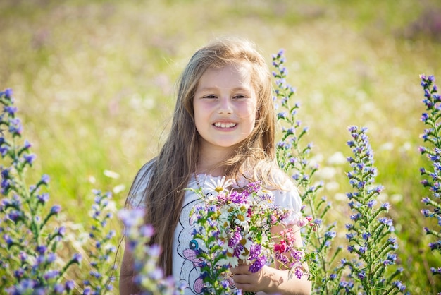Porträt eines süßen kleinen glücklichen siebenjährigen Mädchens mit Blüte blüht Lupinen auf einem Feld in der Natur im Freien.