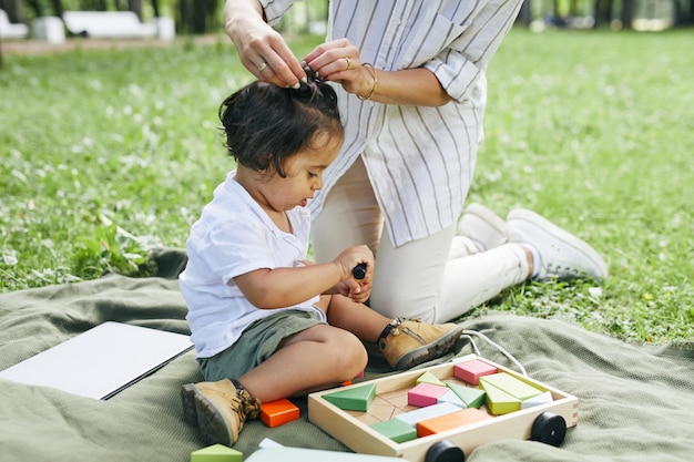Porträt eines süßen kleinen Jungen, der mit Spielzeug im Park spielt, während er auf grünem Gras sitzt und den Sommer genießt...