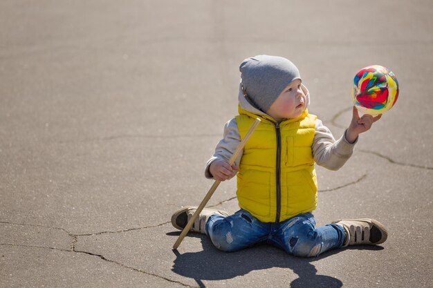 Porträt eines süßen kleinen Kleinkindes, das auf Asphalt sitzt und mit Ballon spielt Kind im Freien