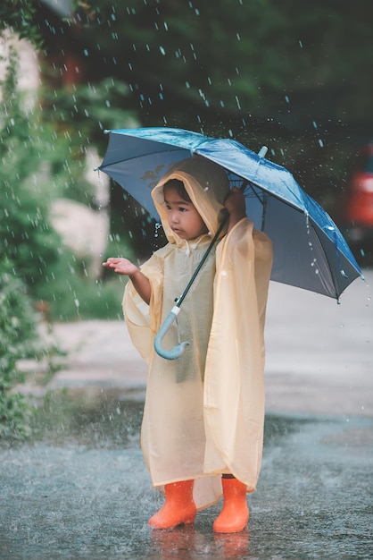 Porträt eines süßen kleinen Mädchens, das einen Regenmantel trägt und einen Regenschirm auf die Menschen in Thailand hält