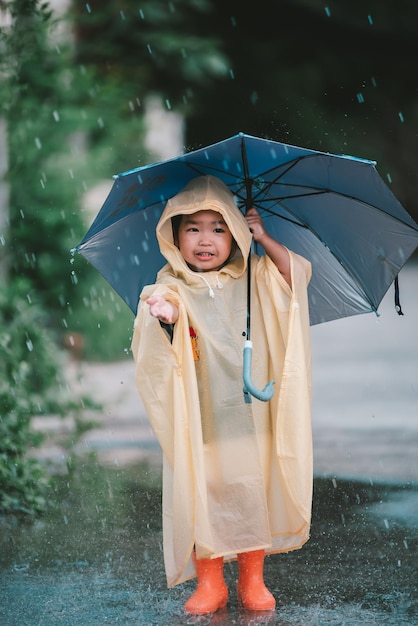 Porträt eines süßen kleinen Mädchens, das einen Regenmantel trägt und einen Regenschirm auf die Menschen in Thailand hält