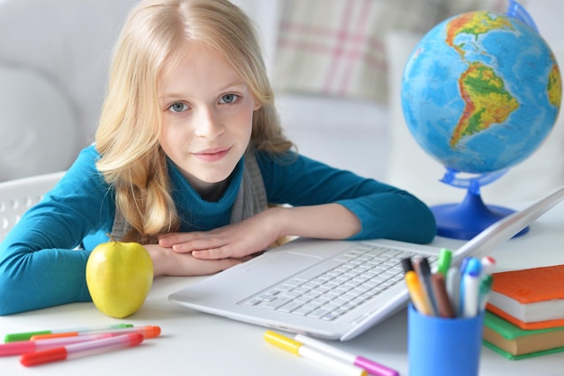 Porträt eines süßen kleinen Mädchens, das mit Laptop am Tisch sitzt