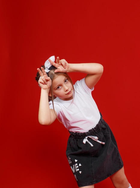Porträt eines süßen kleinen Mädchens in einem weißen T-Shirt und schwarzem Rock auf rotem Grund.