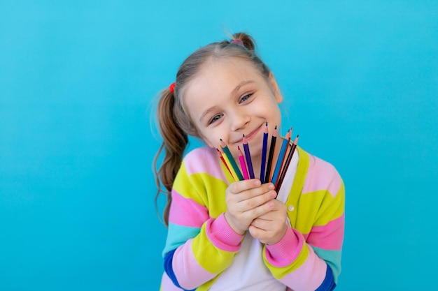 Porträt eines süßen kleinen Mädchens mit Buntstiften in einer gestreiften Jacke Das Konzept der Bildung und Zeichnung Fotostudio blauer Hintergrund Platz für Text