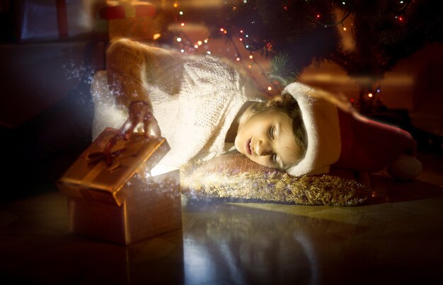 Porträt eines süßen lächelnden Mädchens, das auf dem Boden liegt und in eine magische leuchtende Schachtel schaut