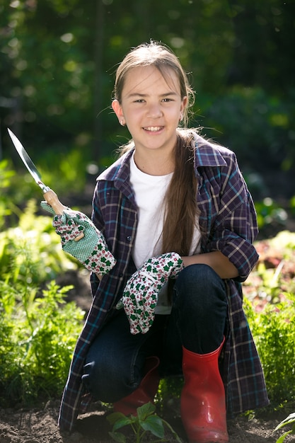Porträt eines süßen lächelnden Mädchens in Handschuhen und Gummistiefeln, das im Garten posiert