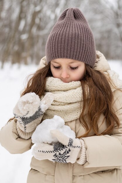 Porträt eines süßen sechsjährigen Mädchens in Winterjacke und Hut, das in Fäustlingen einen Schneeball formt