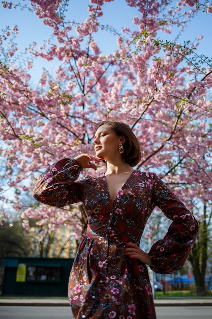 Porträt eines süßen und schönen Mädchens in einem Kleid im Garten mitten in blühender Kirschblüte. Frühlings- und Sonnenzeit. Unscharfer Hintergrund und ausgewählter Fokus.