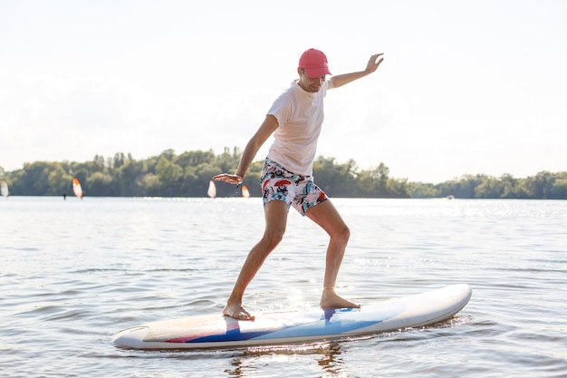 Porträt eines Surfers mit einem SUP-Board am Strand. Junger Mann auf Paddleboard im Morgengrauen. Das Konzept des Extremsports. Männlicher Surfer-Lebensstil.