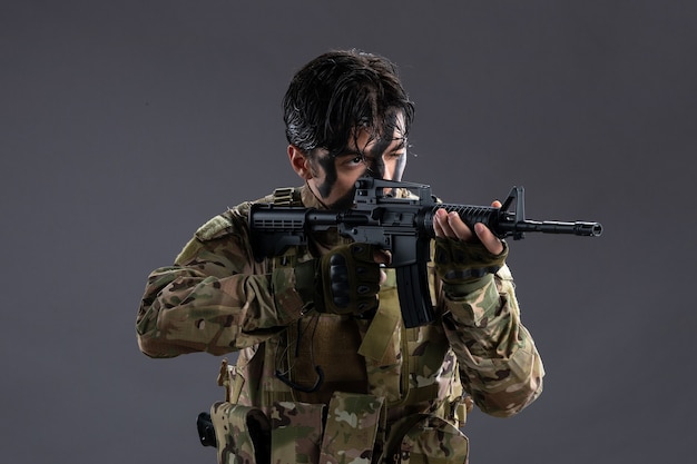 Porträt eines tapferen Soldaten in Militäruniform mit Maschinengewehr an dunkler Wand