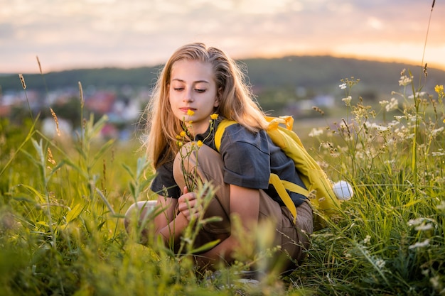 Porträt eines Teenager-Mädchens mit einem Rucksack, der an einem Sommerabend vor dem Hintergrund einer Landschaft und eines Sonnenuntergangs reist.