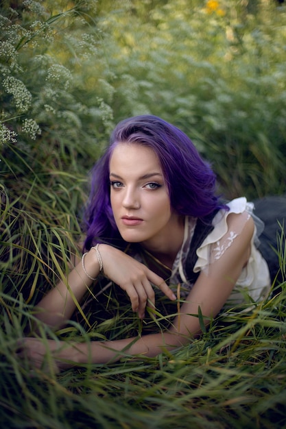 Porträt eines Teenager-Mädchens mit lila Haaren und einem Ohrring in der Nase, das in der Natur im Gras liegt