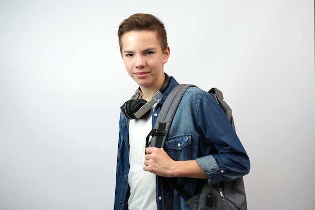 Porträt eines Teenager-Schülers, der in die Kamera schaut. Glücklicher Schuljunge mit Rucksack und Buch auf weißem Hintergrund.