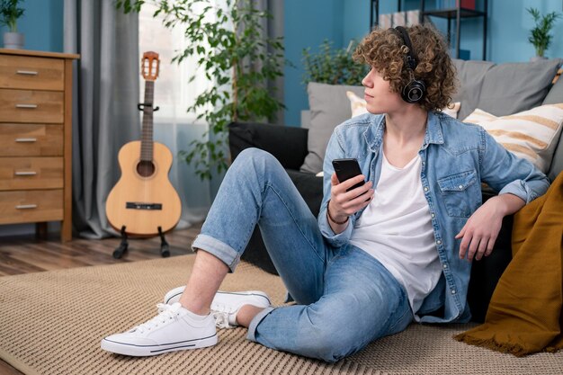 Porträt eines Teenager-Studenten, der Musik lernt, sitzend auf dem Bodenteppich in seinem Wohnzimmer zu Hause t