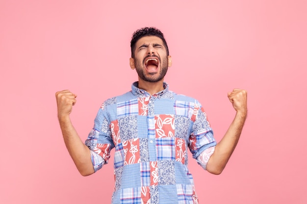 Porträt eines überglücklichen gutaussehenden Mannes mit Bart im Freizeithemd, der mit erhobenen Fäusten eine gewinnende Geste ausdrückt und den Sieg schreiend feiert Studioaufnahme im Innenbereich isoliert auf rosa Hintergrund